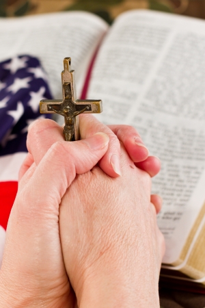 adult female hands holding a crucifix with a camouflage background and an open bible with an American flag to the sideの写真素材