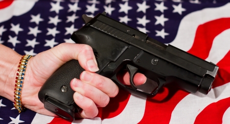 female hand holding a handgun over an american flagの写真素材