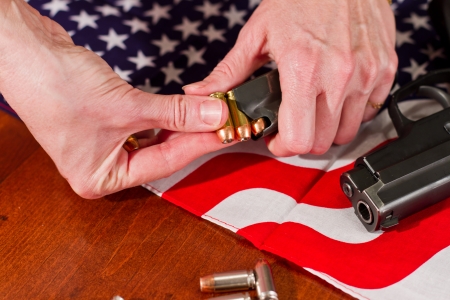 female hands loading a hand gun with hallow point bullets and an american flag in the backgroundの写真素材