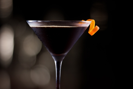 dark cocktail garnished with an orange twist on a dark bar settingの写真素材