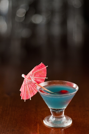 small tropical blue martini garnished with a cherry and a parasolの写真素材