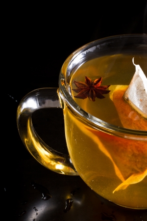 hot cup of tea served on a dark setting with steam and an anise star floating with the tea bagの写真素材