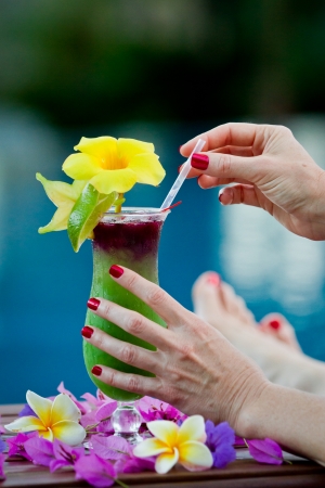 close up of a tropical cocktail served pool side with female hands holding the glass in the rainforest of Belizeの写真素材