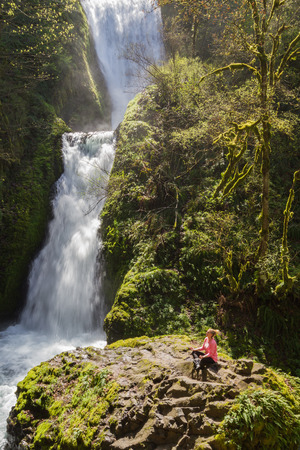 attractive woman sitting in on a rock with bridal veil falls on the side, Oregon USAの写真素材