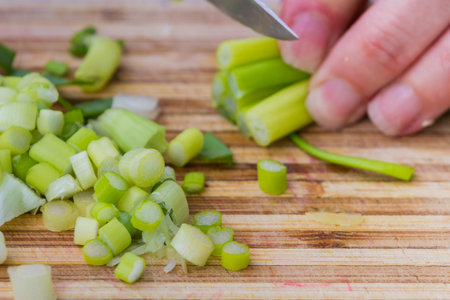 closeup of hand in motion slicing  fresh clean leeks or green onions on a cutting boardの写真素材