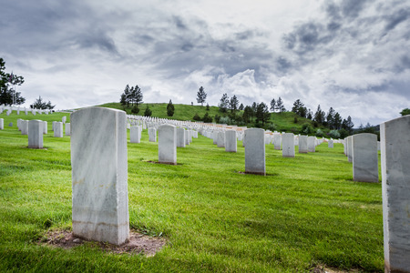 rows of tombstones in a military graveyard with bright green spring grass and dramatic storm cloudsのeditorial素材