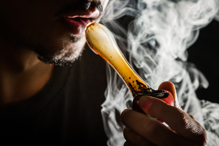 studio shoot with model simulating smoking pot with a pipe in a dark high contrast imageの写真素材