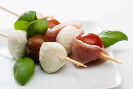 close up of a fresh mozzarella and tomato appetizer with basil and proscuitto on a white plateの写真素材