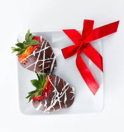 hand dipped and decorated chocolate covered strawberries with a red bow on a white plateの写真素材