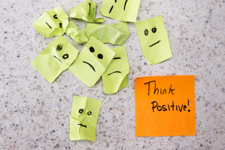 concept for a positive attitude with small crumbled up sad faces and a note with the phrase think positiveの写真素材