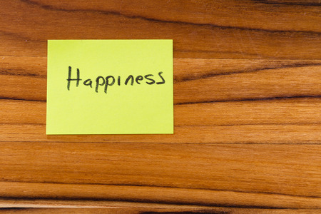 sticky note on a wooden desk with the word happiness written  on itの写真素材