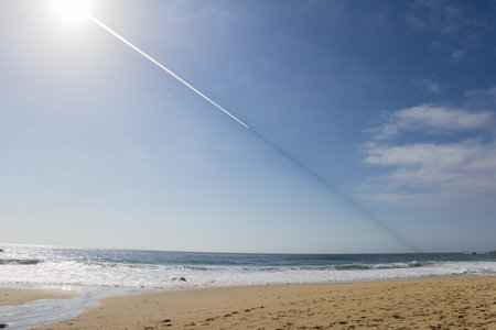 a strange trail in the sky over the California coast, with a white trail behind the plane and a dark...