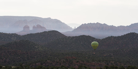 Aerial view of Sedona Arizona with a Hot air balloon soaring thru the landscape on a smoky morningの写真素材