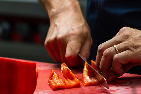 close up of a chefs hands slicing sweet bell peppers on a red cutting boardの写真素材