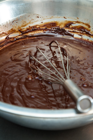 close up of melted chocolate in a large bowl with a whisk for mixingの写真素材