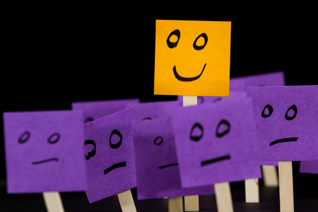 conceptual image using sticky notes with hand drawn faces on them isolated on a black backgroundの写真素材