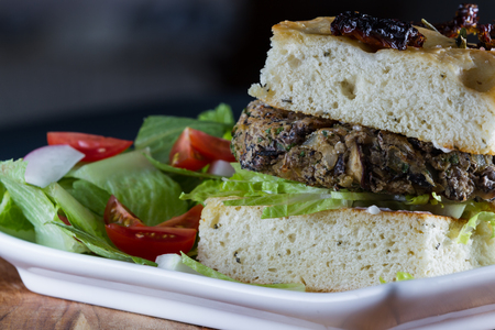 close up of a home prepared vegetarian meal consisting on a bean burger on sundries tomato foccacia served with a saladの写真素材
