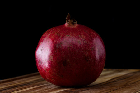 close up of a whole organic raw pomegranate over a black background
