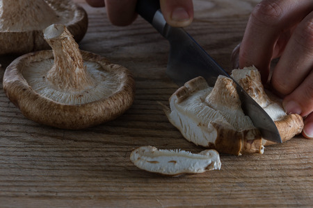 close up of a chefs hands slicing raw mushrooms on a wooden cutting boardの写真素材