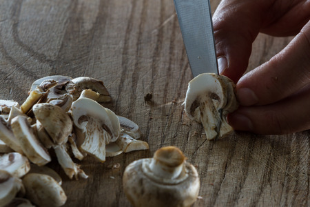 close up of a chefs hands slicing raw mushrooms on a wooden cutting boardの写真素材