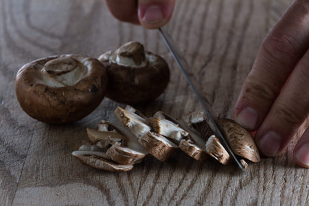 close up of a chefs hands slicing raw mushrooms on a wooden cutting boardの写真素材
