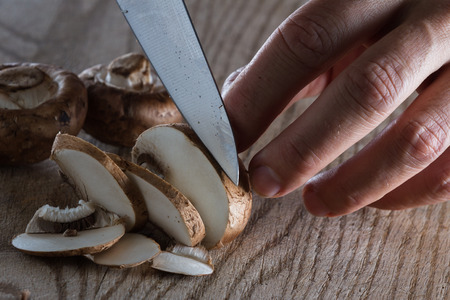 close up of a chefs hands slicing raw mushrooms on a wooden cutting boardの写真素材