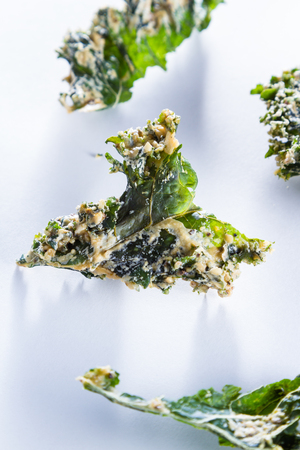 close up of a kale chip covered with melted parmesan cheese and spices on a white backgroundの写真素材