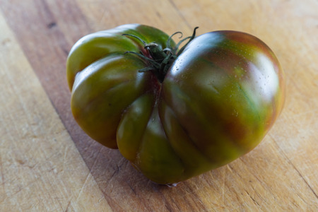 close up of a greenish heirloom tomato on a wooden cutting boardの写真素材