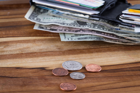 close up of a wallet with American Dollars sticking out and change on a wooden tableの写真素材