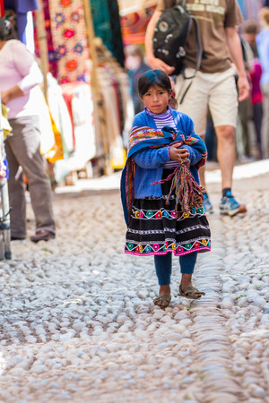 Pisac, Peru - May 15: Adorable native Quechua girl walking the alleyways selling hand made souvenirs in the Sacred Valley Market. May 15 2016, Pisac Peru.のeditorial素材
