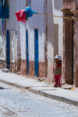 Maras Peru -May 18 : Young boy standing outside of his door eating fresh fruit with a traditional plastic flag indicating the Chicha is ready. May 18 2016, Maras Peru.のeditorial素材