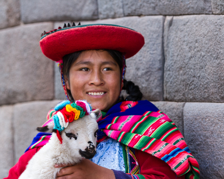 Cusco, Peru - May 14 : Jenni, a young woman dressed in colorful traditional native Peruvian closing holding a baby Lamb with Inca walls in the background. May 14 2016, Cusco Peru.のeditorial素材