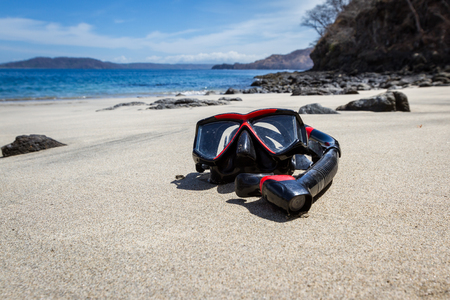 wide angle close up of a snorkeling mask and tube on a relaxing beach with blue water in the background.の写真素材