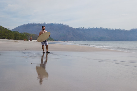 young man holding his skim board in Playa Cabuyal, Costa Rica on a smoky day due to prescribed burns in the area.のeditorial素材