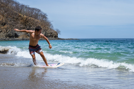 young man skim boarding in Playa Calzon de Pobre, Costa Rica on a beautiful sunny day.の写真素材