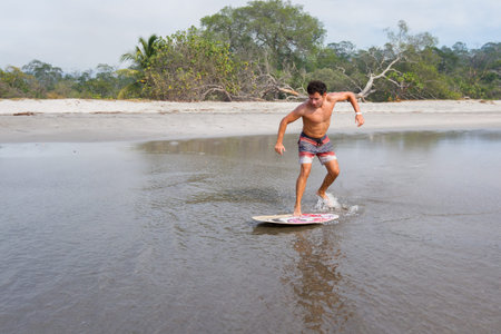 young man skim boarding in Playa Cabuyal, Costa Rica on a a smoky day due to prescribed burns in the...