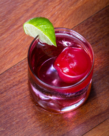 refreshing drink with a red ice ball releasing flavor into the cocktail as it melts and chills the...