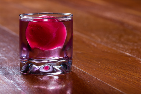 refreshing drink with a red ice ball releasing flavor into the cocktail as it melts and chills the beverageの写真素材