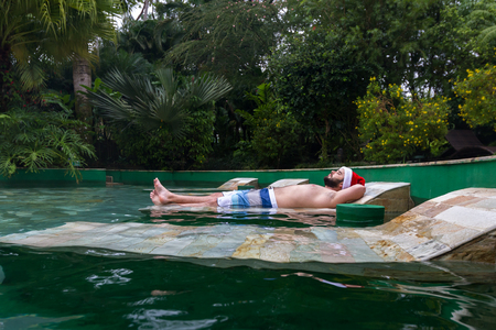 young man laying down in natural hot springs in tropical Costa Rica with a red holiday hatのeditorial素材