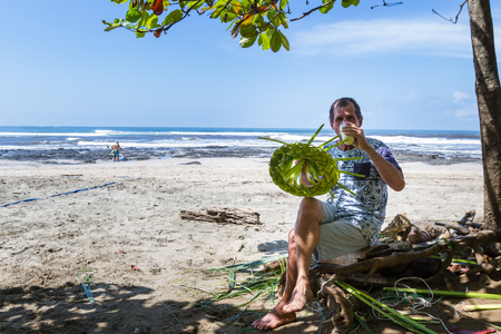 Langosta Beach, Costa Rica - October 12: Local man making hats with palm leaves on the beach and enjoying a pina colada. October 12 2017, Langosta Beach Costa Rica.のeditorial素材