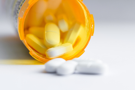 close up of a group of white tablets with an out of focus prescription bottle in the backgroundの写真素材
