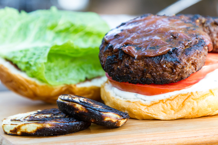 grilled plant based burger served with a home made sauce and fresh tomato and lettuce on a wooden cutting boardの写真素材