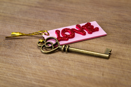 conceptual image using an old key with a pink tag with red glitter letters spelling the word love over a wooden backgroundの写真素材