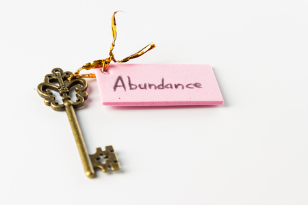 Close up of an ornamental key with the word abundance hand written on a pink tag isolated on a white backgroundの写真素材