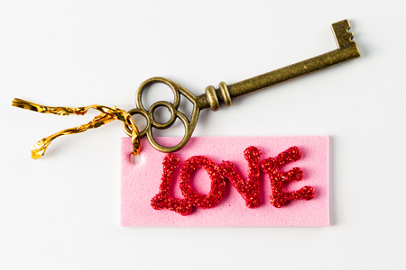 Close up of an ornamental key with a tag and the word Love in glitter letters isolated on a white backgroundの写真素材