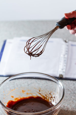melted chocolate in a glass bowl with a whisk and an open recipe book out of focus