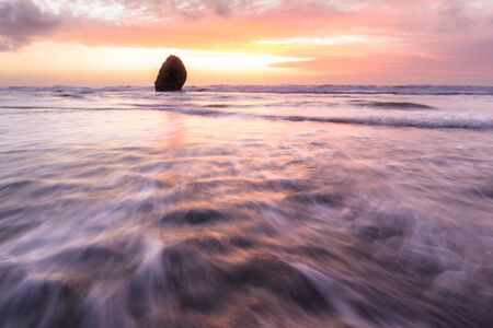 Sunset scene in Gold Beach Oregon with colorful clouds and waves adding reflected color to wet sand and rocksの写真素材