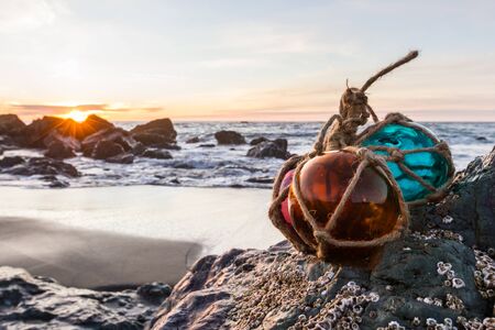 Sunset in the Oregon coast with colorful glass floats on a rock and a sandy beach and the ocean in the backgroundの写真素材