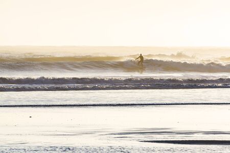 Surfing in the cold pacific waters of the Oregon coast as the sun sets casting a strong backlight adding a glow on the mist and moisture in the airの写真素材