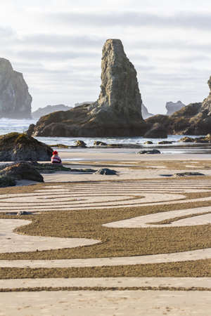 Bandon by the Sea, Oregon / USA - February 21 2020: Person sitting on a rock enjoying the landscape waiting for the labyrinth to open in the beach of Face Rock State Parkのeditorial素材